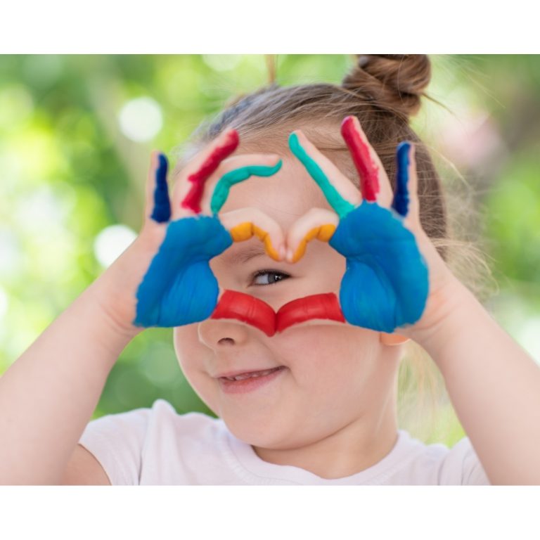 Fröhliches Kind mit bunt bemalten Händen, symbolisiert gesunde Ernährung und Glück