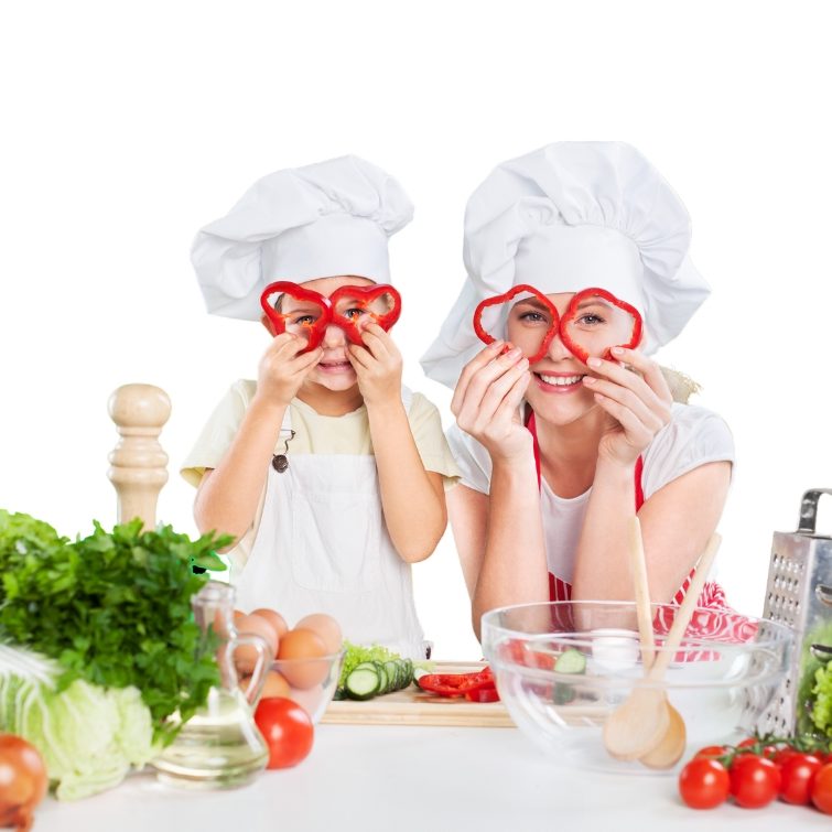 Mutter und Kind in Kochmützen bereiten in der Küche gemeinsam frisches Essen zu.